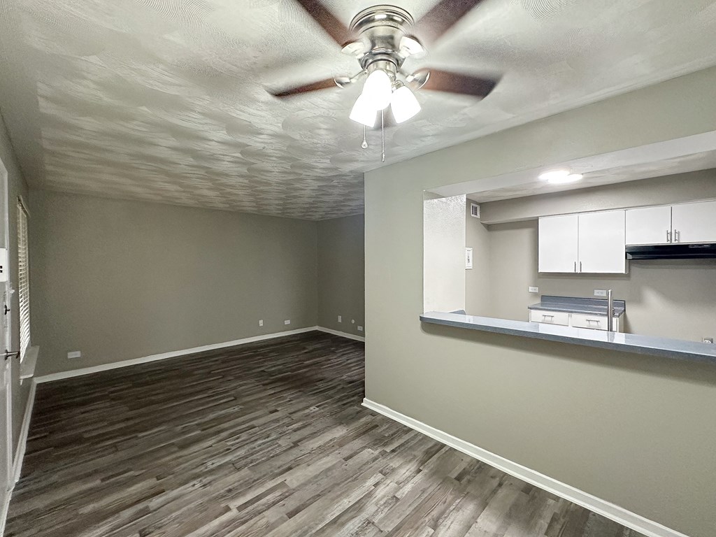 an empty living room with a ceiling fan and a kitchen