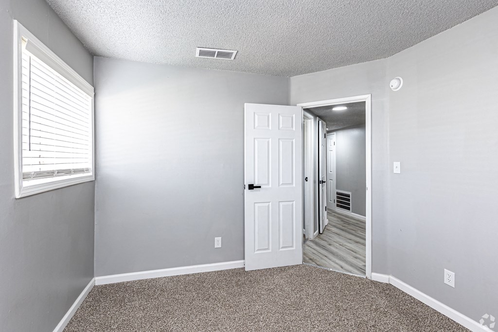 an empty room with a white door and a hallway with a door to a bedroom