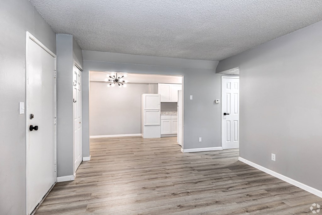 an empty living room and kitchen with white walls and wood flooring