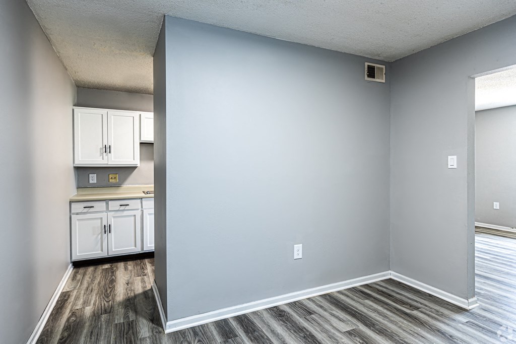 an empty living room and kitchen with white cabinets and a blue wall