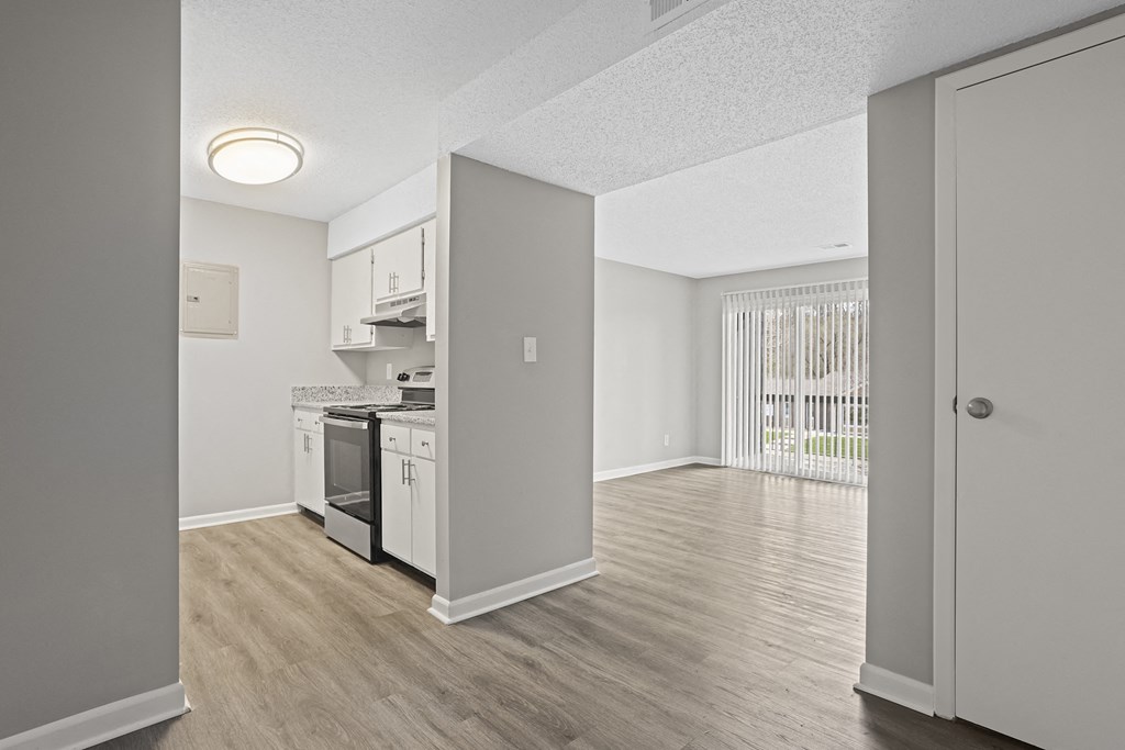 the spacious kitchen and living room of a renovated apartment with white appliances and wood floors