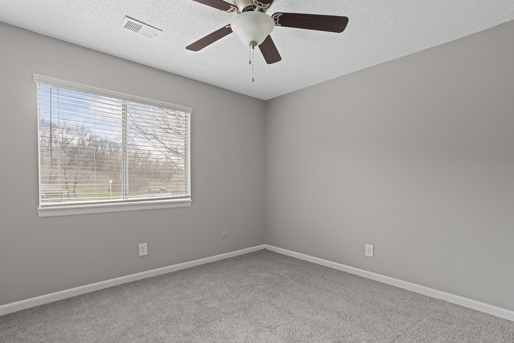 an empty bedroom with a ceiling fan and a window