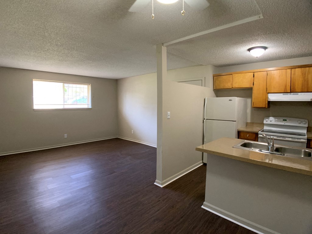 Image of a living room and kitchen with a breakfast bar, refrigerator, sink, and oven.
