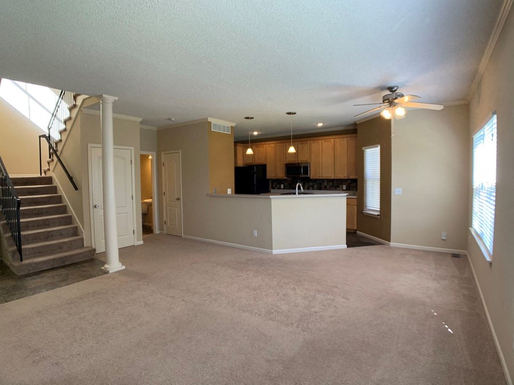an empty living room with a kitchen and a ceiling fan