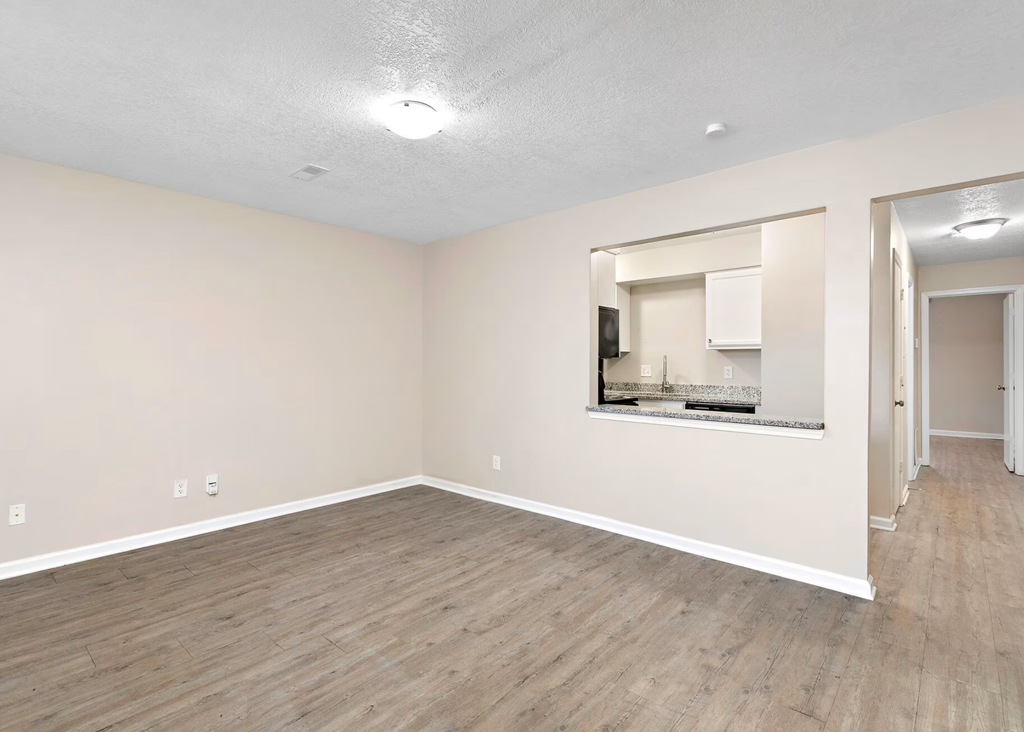 an empty living room with a mirror and a kitchen