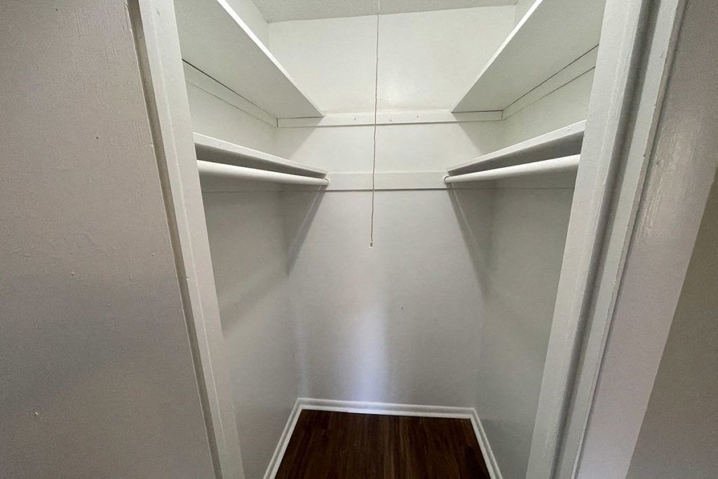 a walk in closet with white shelves and a wood floor