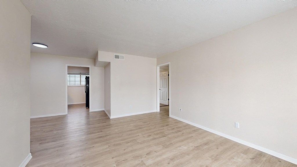 the spacious living room and dining room with hardwood flooring and white walls