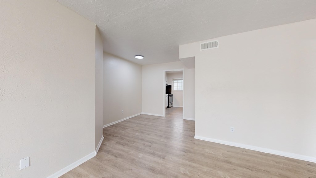 the spacious living room and dining room with white walls and wood flooring