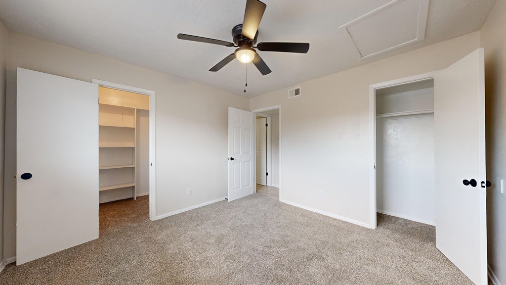 an empty bedroom with a ceiling fan and closet