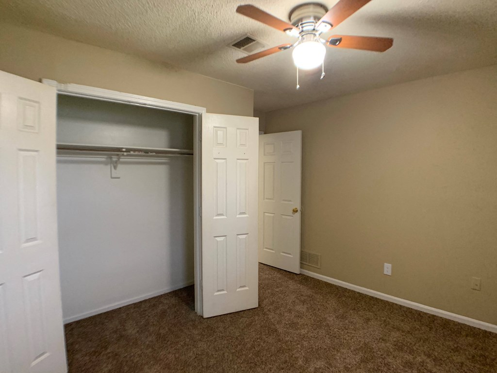 large carpeted bedroom with closet and ceiling fan