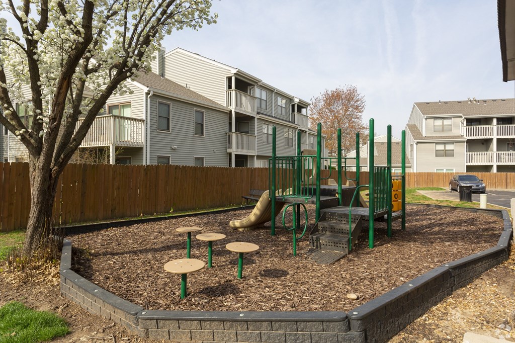 A playground with a green swing set and a tree in the background.