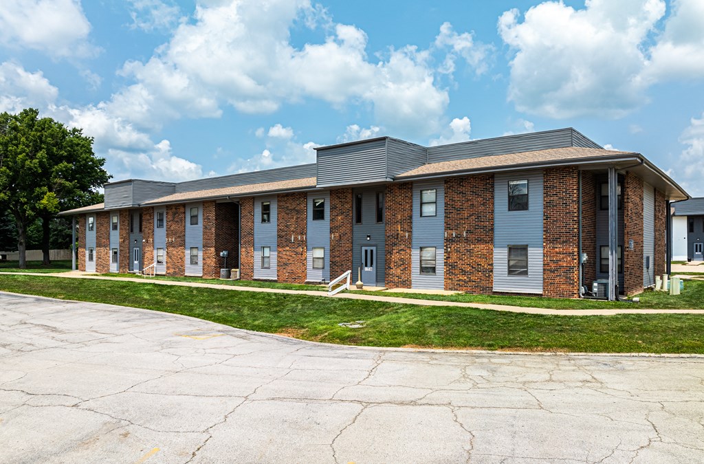the front of a brick building with a sidewalk and grass
