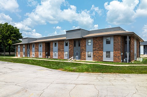 the front of a brick building with a sidewalk and grass