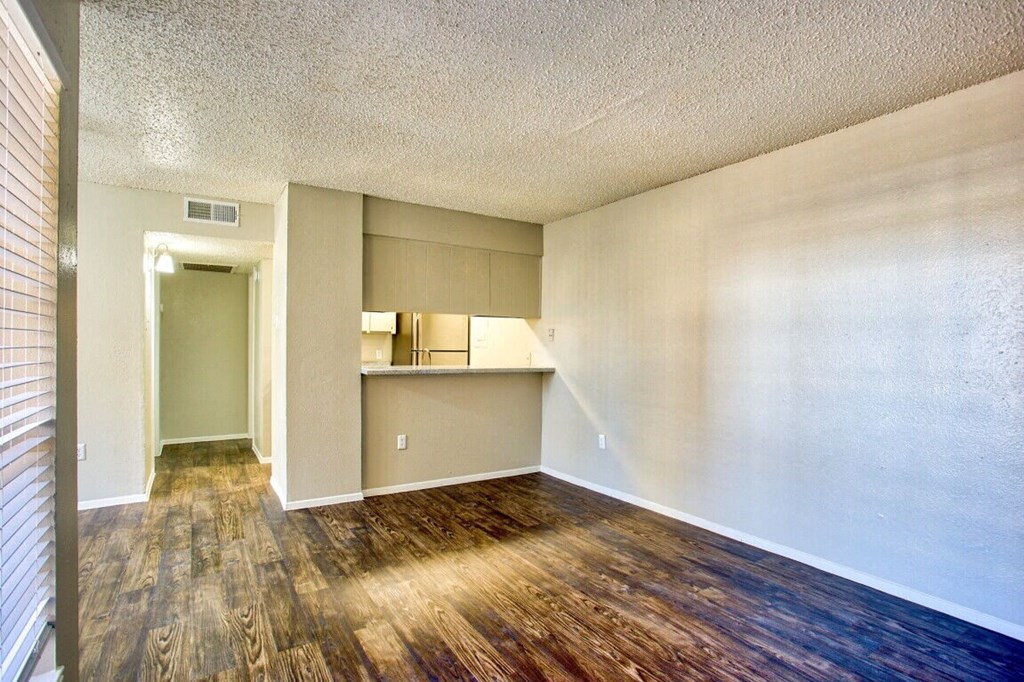 an empty living room with wood flooring and a kitchen
