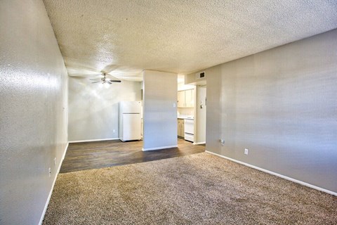 an empty living room with a ceiling fan and a kitchen
