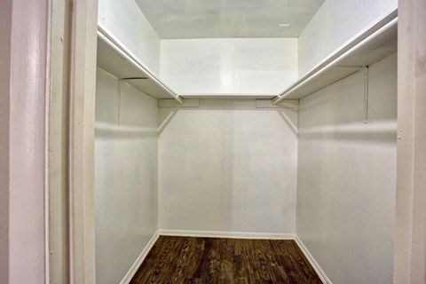 a walk in closet with white walls and a wood floor