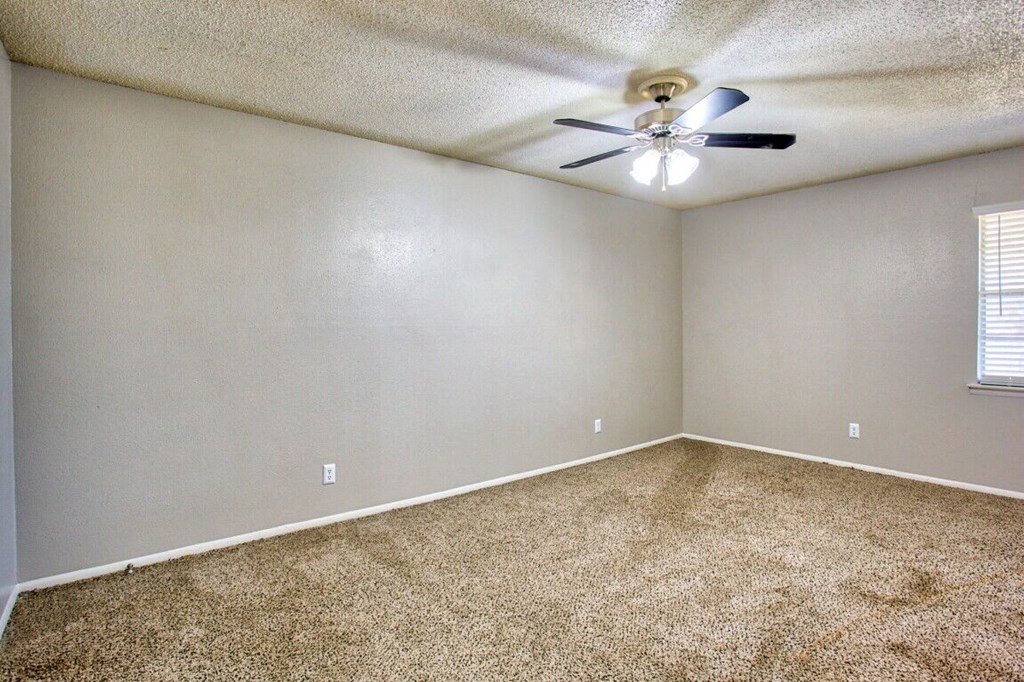 an empty living room with a ceiling fan and carpet
