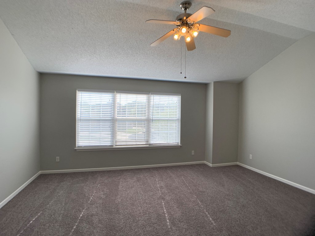 Large carpeted bedroom with ceiling fan and window