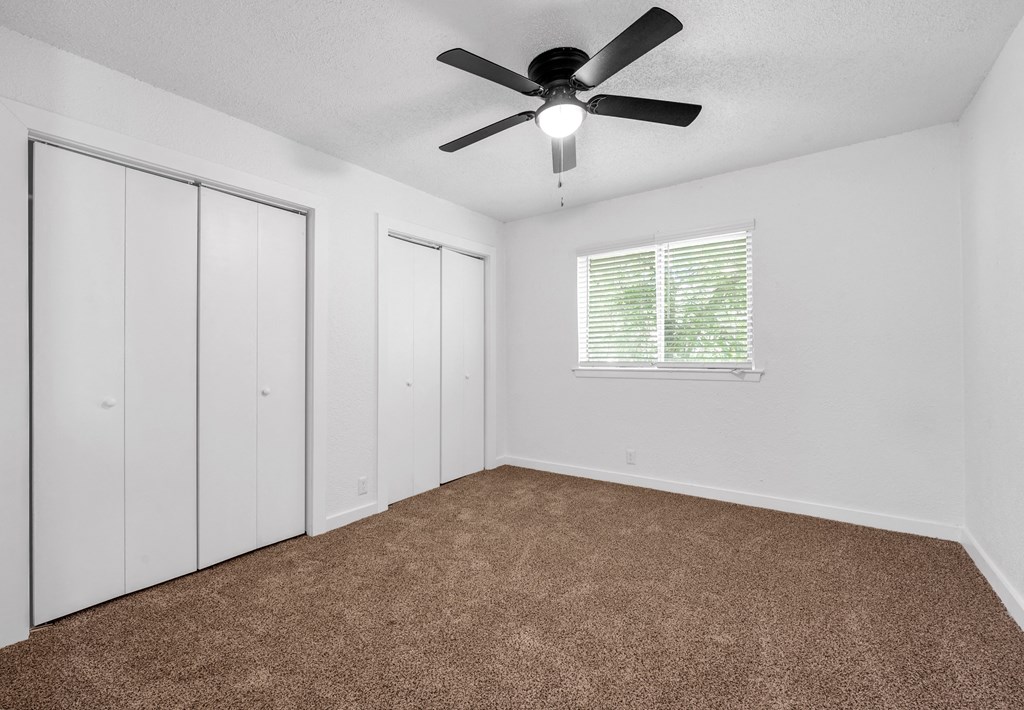 an empty bedroom with a ceiling fan and white closets