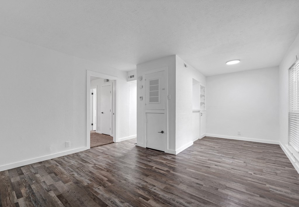 the living room of an apartment with white walls and wood flooring