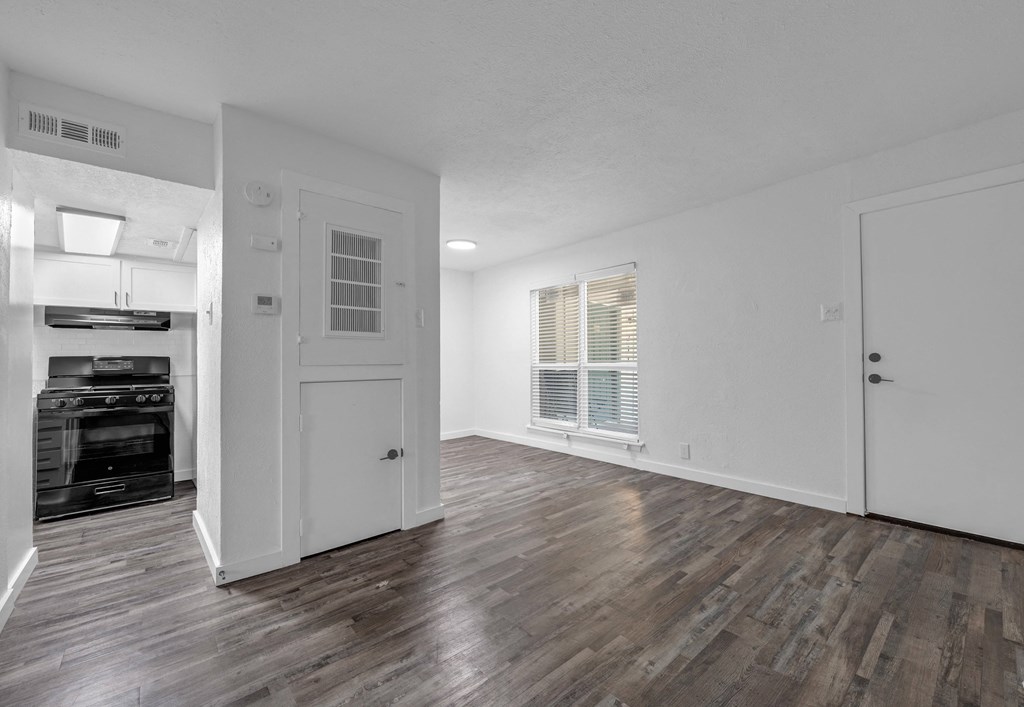 the living room and kitchen of an apartment with white walls and wood flooring