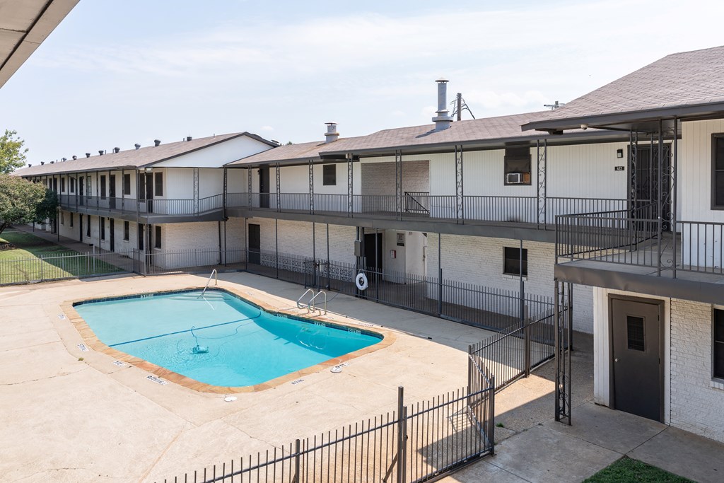 A pool is surrounded by a fence in front of a building.