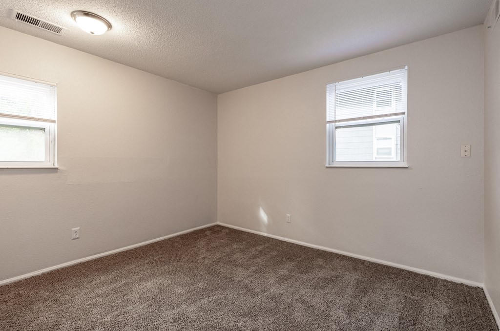 a bedroom with two windows and a carpeted floor
