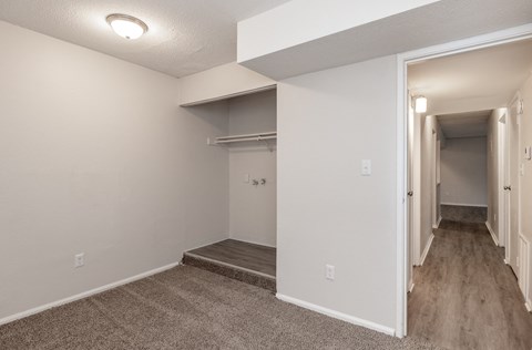 the spacious living room and hallway of an apartment with white walls and wood flooring