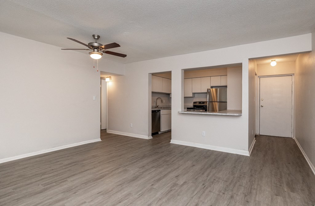 a living room with a ceiling fan and a kitchen in the background