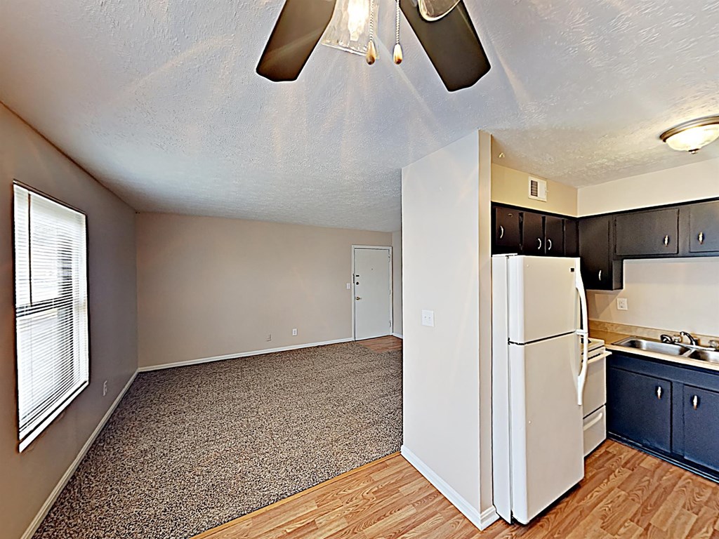 an empty living room with a kitchen and a refrigerator