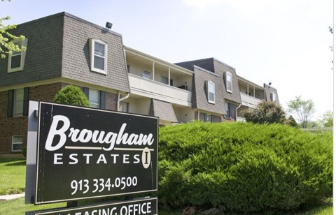 A sign for Brougham Estates in front of apartment buildings.