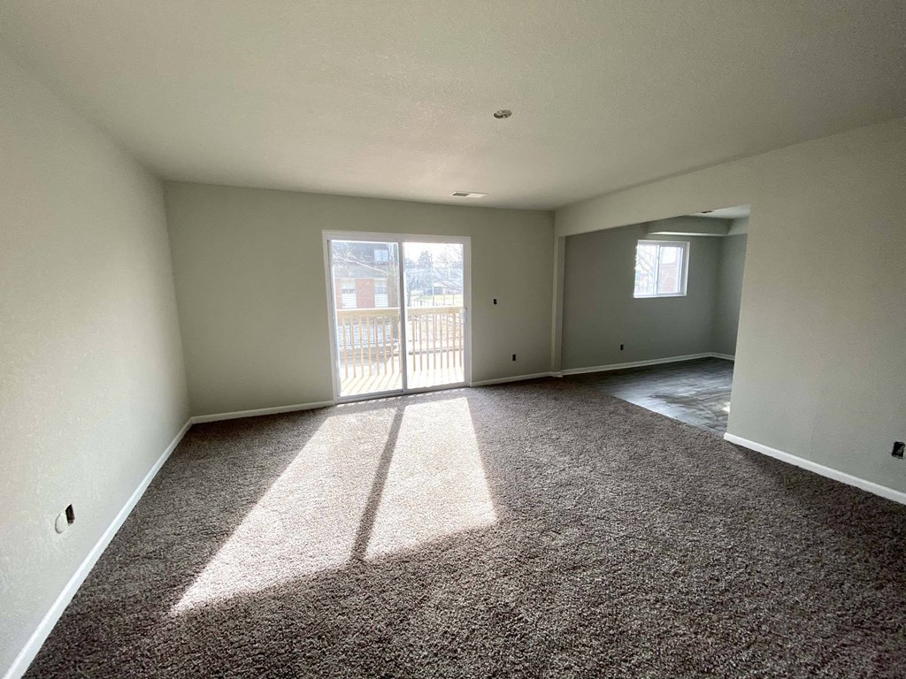 A large empty room with a carpeted floor and a view of a balcony through the door.