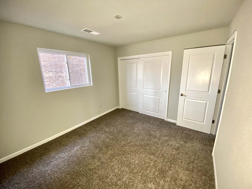 A room with carpeted floor, two doors, and a window with blinds.