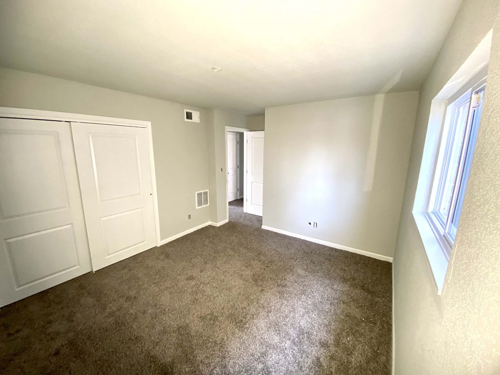 A room with carpeted floor, two doors, and a window.