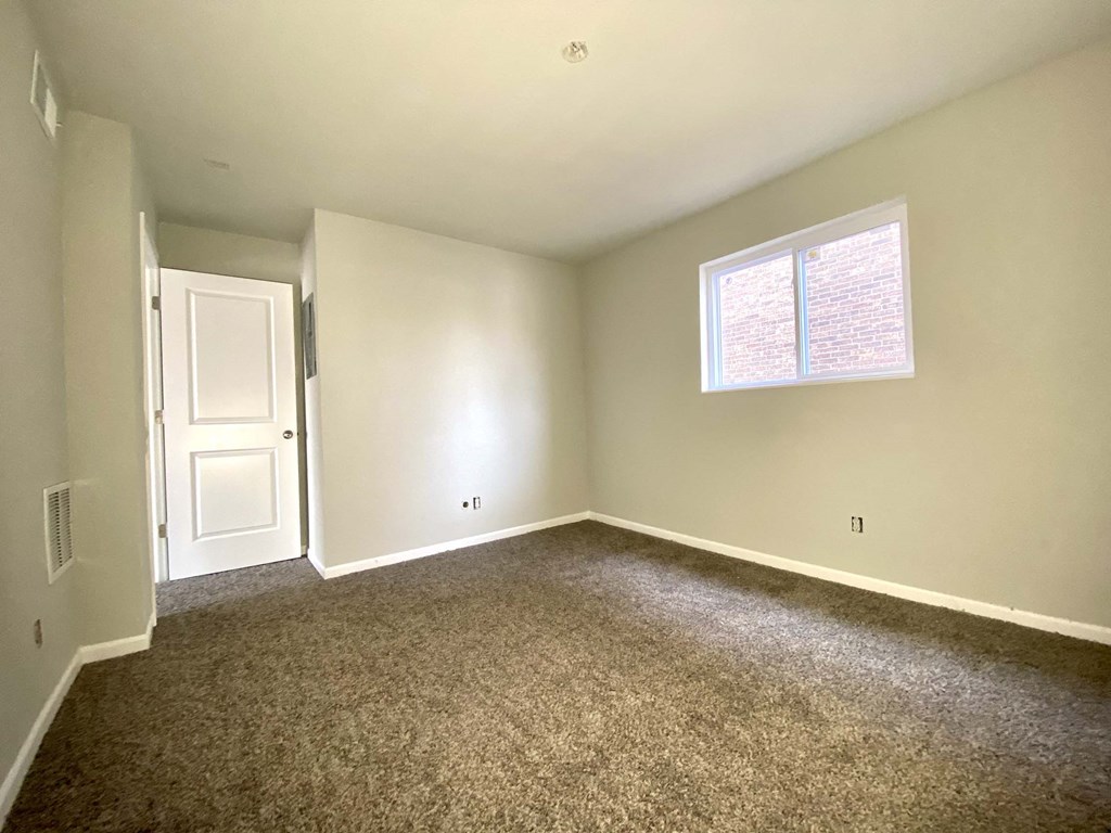 A room with a carpeted floor, a door, and a window with blinds.