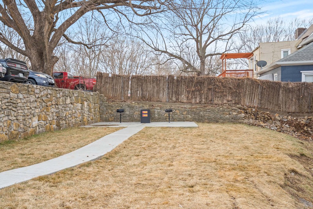 A backyard with a stone wall and a white pathway.