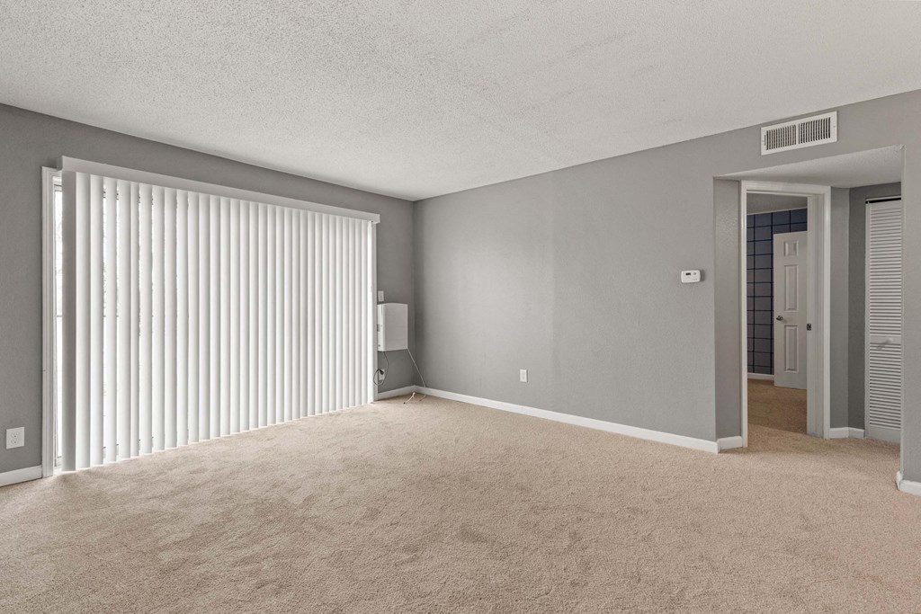 A room with a carpeted floor and a window with blinds.