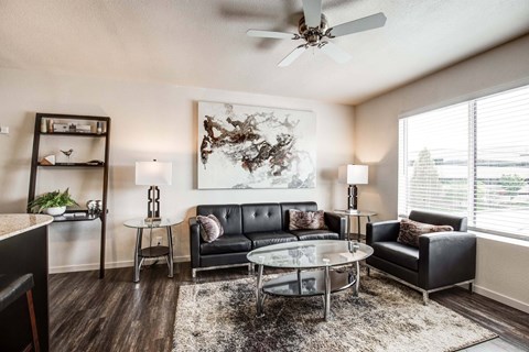 A living room with a black couch, a glass coffee table, and a ceiling fan.