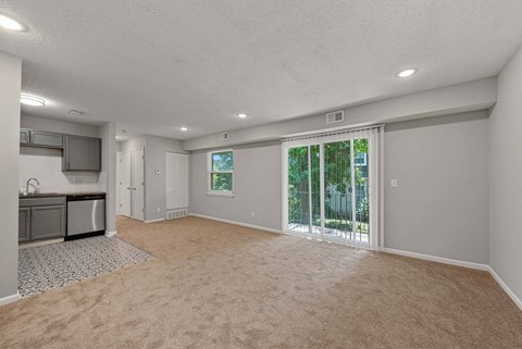 A spacious room with a carpeted floor and sliding glass doors leading to a backyard.