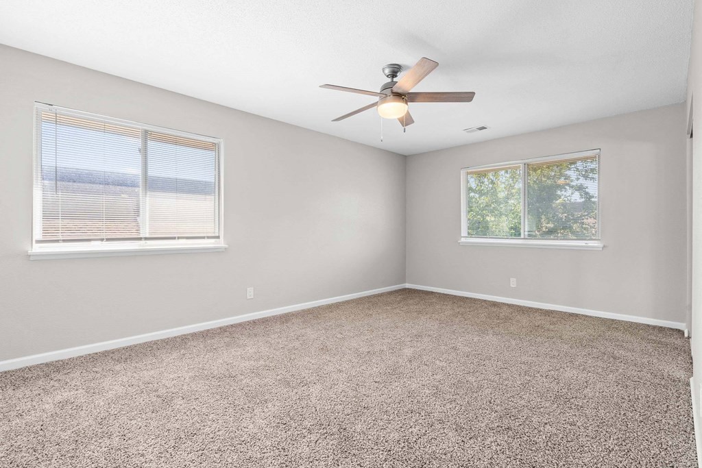 A room with a ceiling fan and two windows.