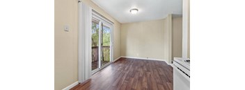 A room with a wooden floor and a sliding glass door leading to a balcony.