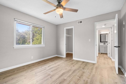A room with a ceiling fan and a window with trees visible outside.