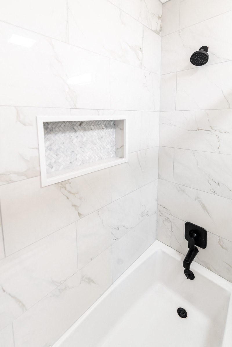A white bathroom with a marble tile wall and a white sink.