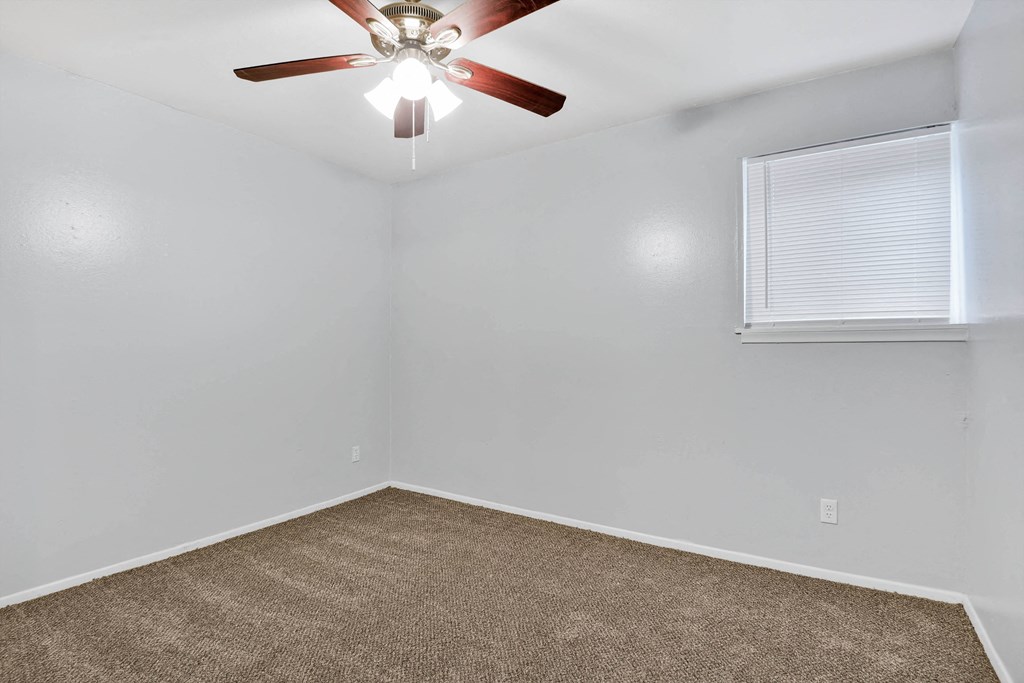 large carpeted room with ceiling fan and window