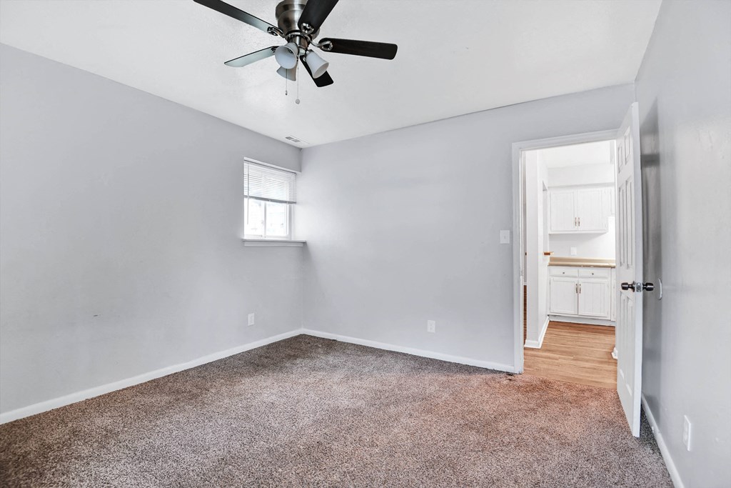 large carpeted room with ceiling fan and window