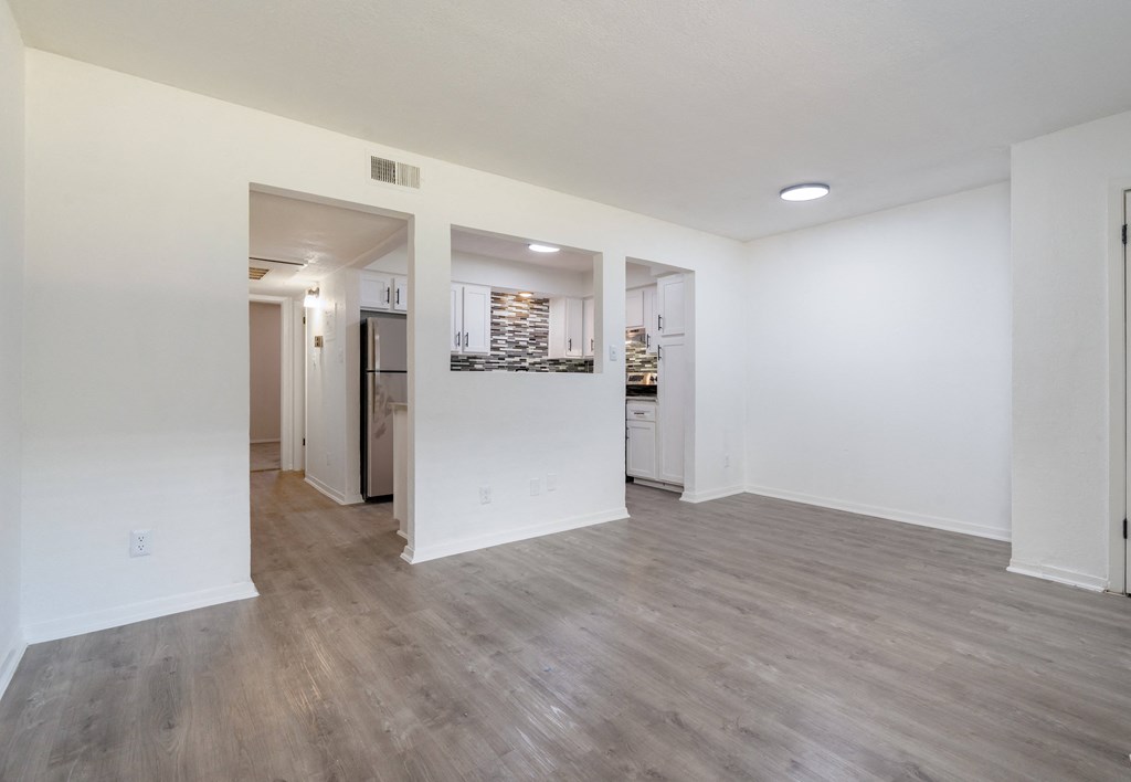 an empty living room and kitchen with white walls and wood flooring