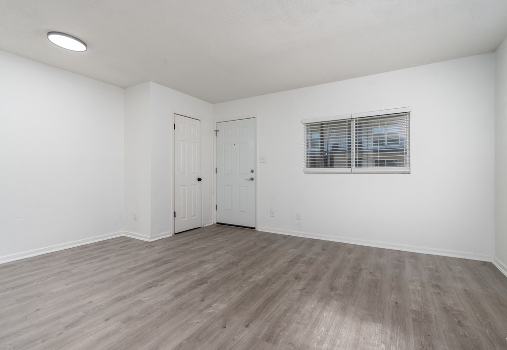 the living room of an apartment with white walls and wood flooring