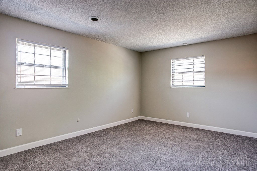 an empty bedroom with two windows and carpeting