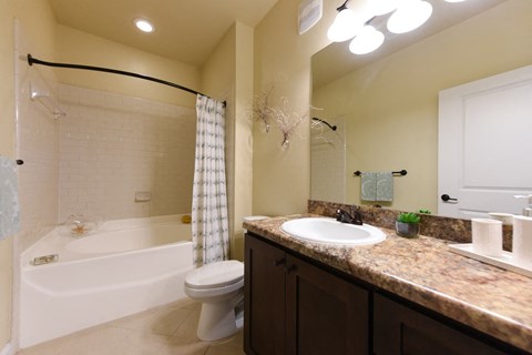 A bathroom with a white toilet, a bathtub with a shower curtain, and a sink with a mirror above it at Cabana Club - Galleria Club Apartments, Florida
