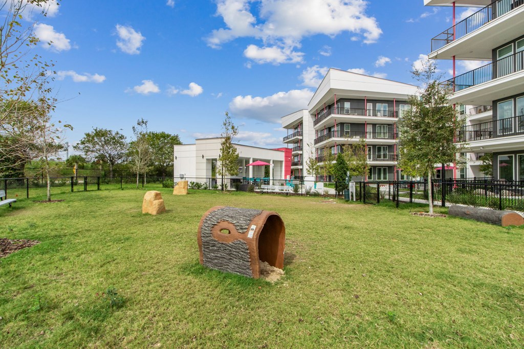 A playground with a wooden tunnel in the middle of a grassy area with apartment buildings in the backgroundat Pinnacle Apartments, Jacksonville, FL